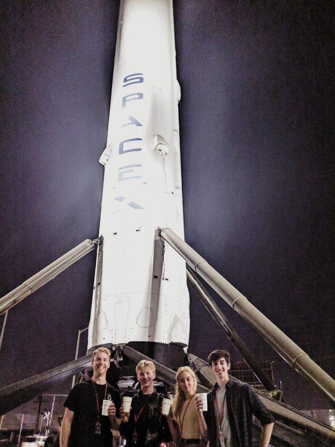 Robotics teacher Andrew Theiss, Erik Anderson ’20, Page Clancy ’ 22 and Dean Reiter ’20 pose in front of the SpaceX rocket with their new SpaceX logo cups in hand. Credit: Printed with permission of Andrew Theiss