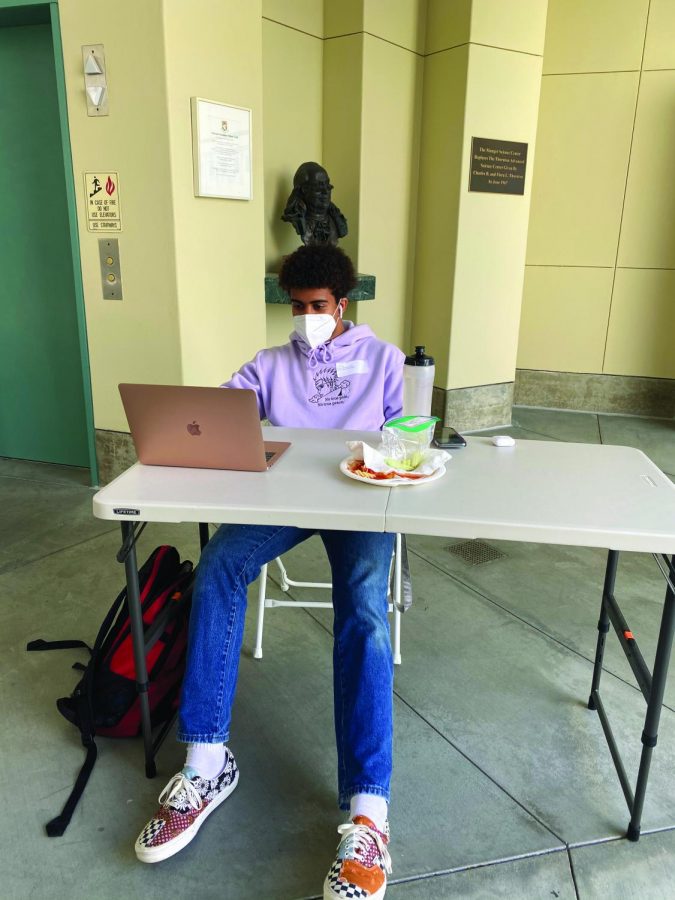Prefect Jason Thompson 22 completes his homework for the day and eats lunch from the cafeteria. He wears the KN95 mask provided to him by the school while sitting near Munger Science Center on March 15.