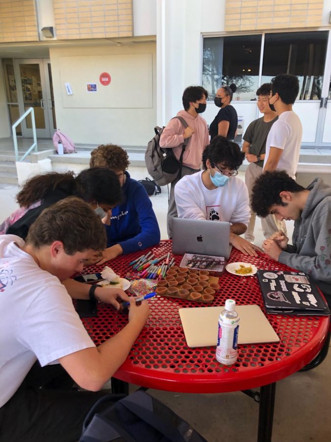 While snacking on South Asian food, Aiden Schiller ’22 paints henna on Rohan Madhogarhia ’22. Meanwhile, Jack Coleman ’22 decorates a diya candle using both Sharpies and stickers.