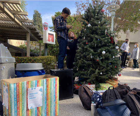 Simon Lee 23 and Cosette Shamonki 23 stand over the presents for the toy drive to hang decorations over the campus Christmas tee.