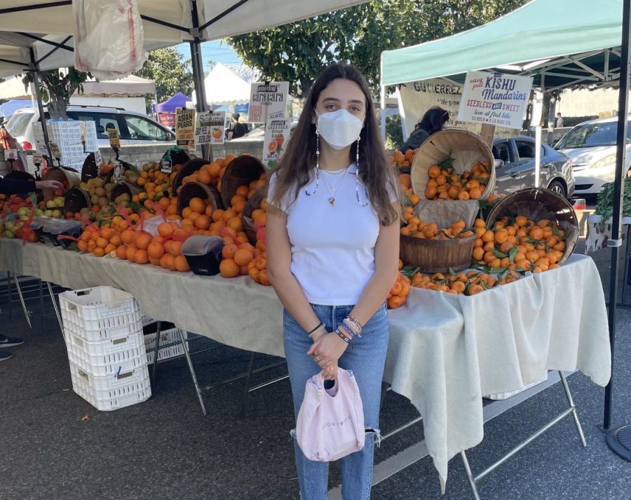 Hannah Carbunaru 24 visits a fruit stand at the Studio City Farmers Market, masked up in front of a table of mandarins.