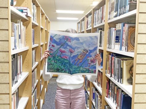 Emma Miller 23 peruses the Stone-Cutters Winter Tabloid while walking through the library shelves.