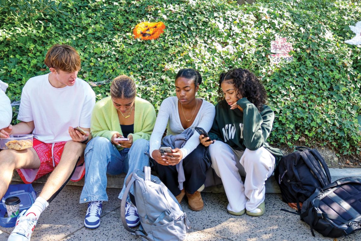 Students on the Quad look at their phones. Starting next year, the school administration will ban phone use during school hours, in a similar policy enacted by the Middle School.