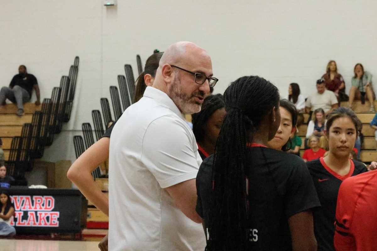 Girls' Volleyball Program Head discusses strategy with his players during a match.